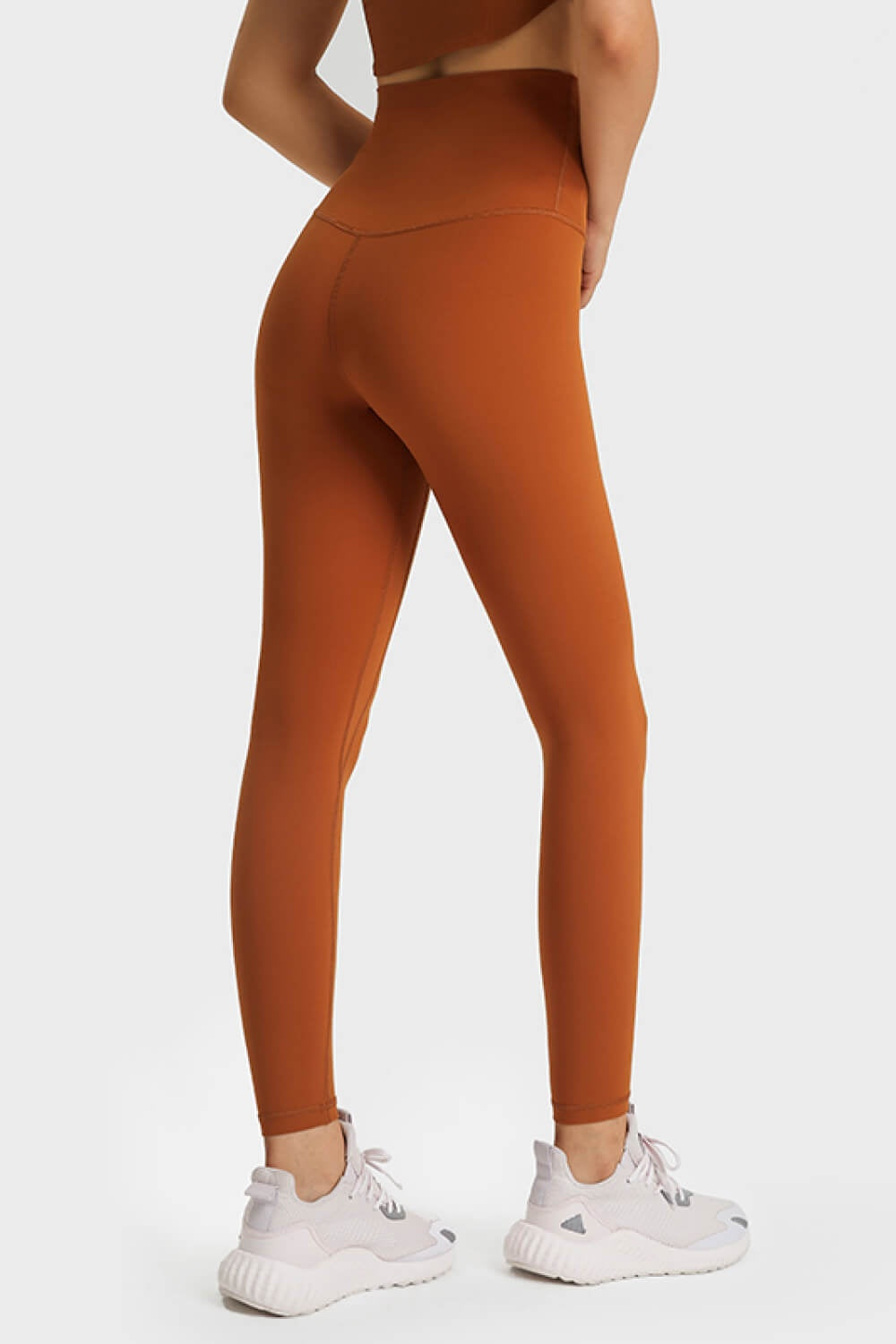 Model stands in a rear three-quarter pose wearing rust-orange ultra soft high waist leggings with a smooth, stretchy, ankle-length silhouette and seamed construction.