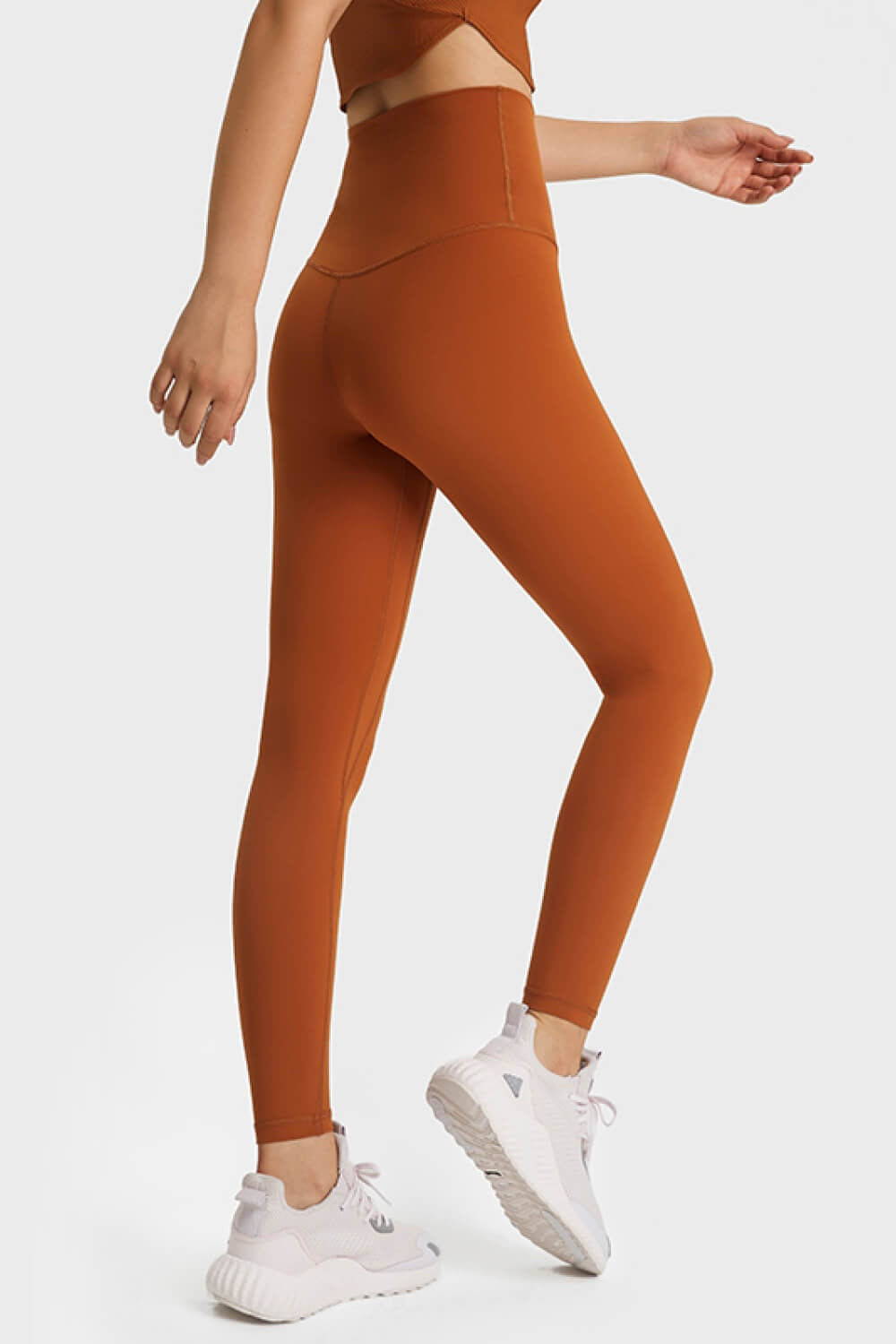 Model poses in rust-orange ultra soft high-waist leggings with a wide elastic waistband, smooth solid finish, close fit, and ankle-length silhouette.