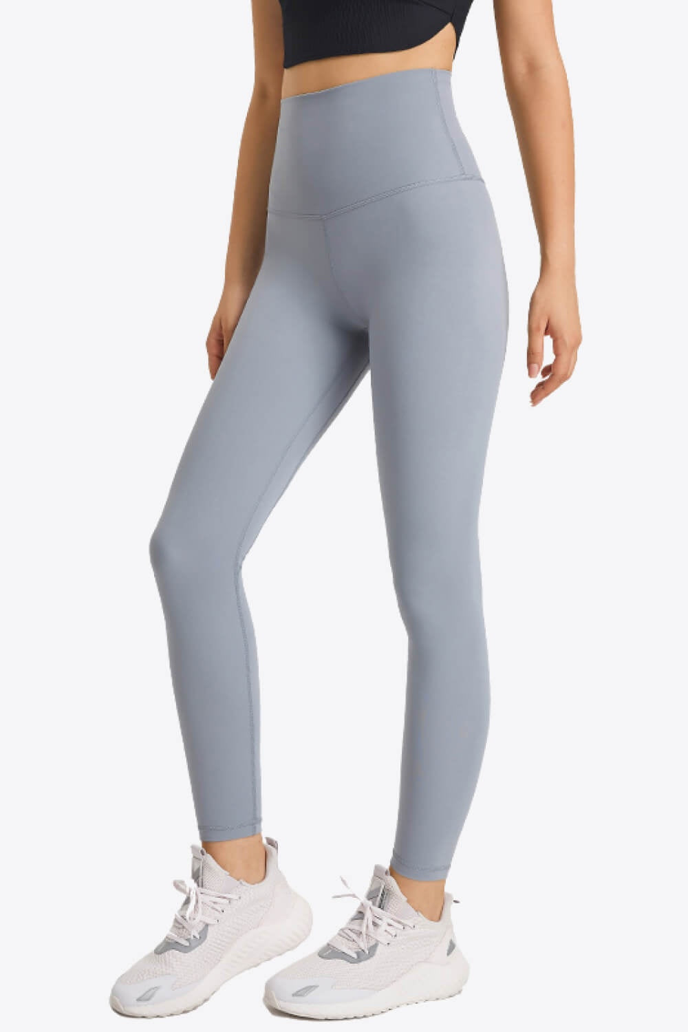 Model wearing light gray high-waist leggings with a wide elastic waistband, smooth fitted silhouette, visible seam construction, and full-length stretch legs.