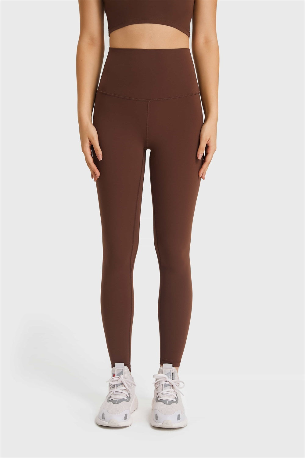 Model stands facing forward in brown Ultra Soft High Waist Leggings with a wide elastic waistband, sleek fitted silhouette, and visible front seams.