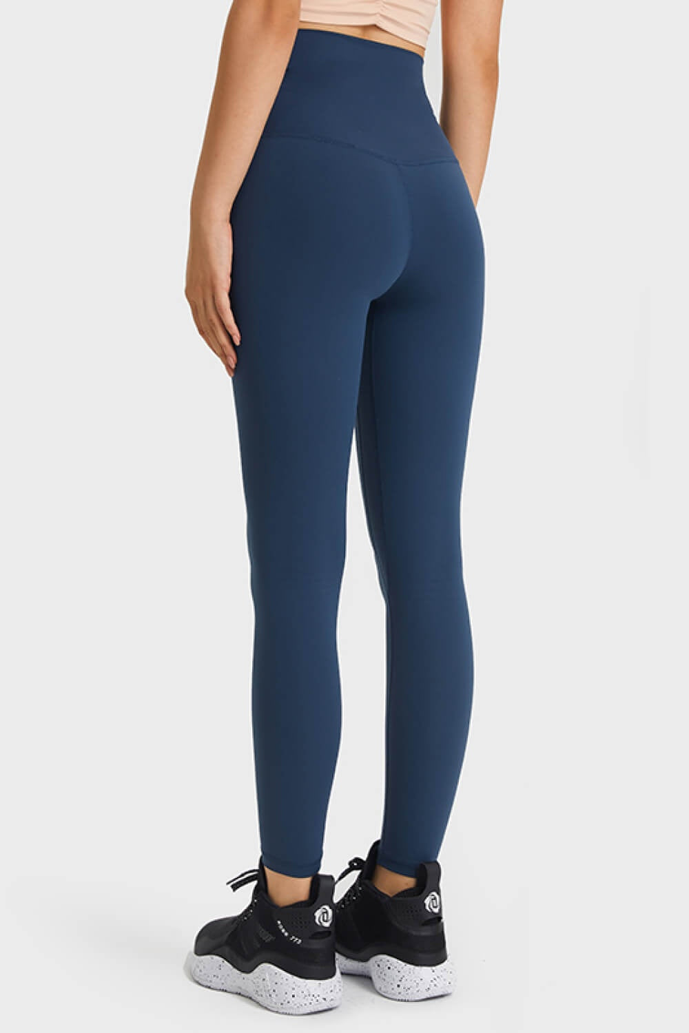A model stands in a back-facing pose wearing solid navy high-waist leggings with a wide elastic waistband and a smooth, close-fitting ankle-length silhouette.