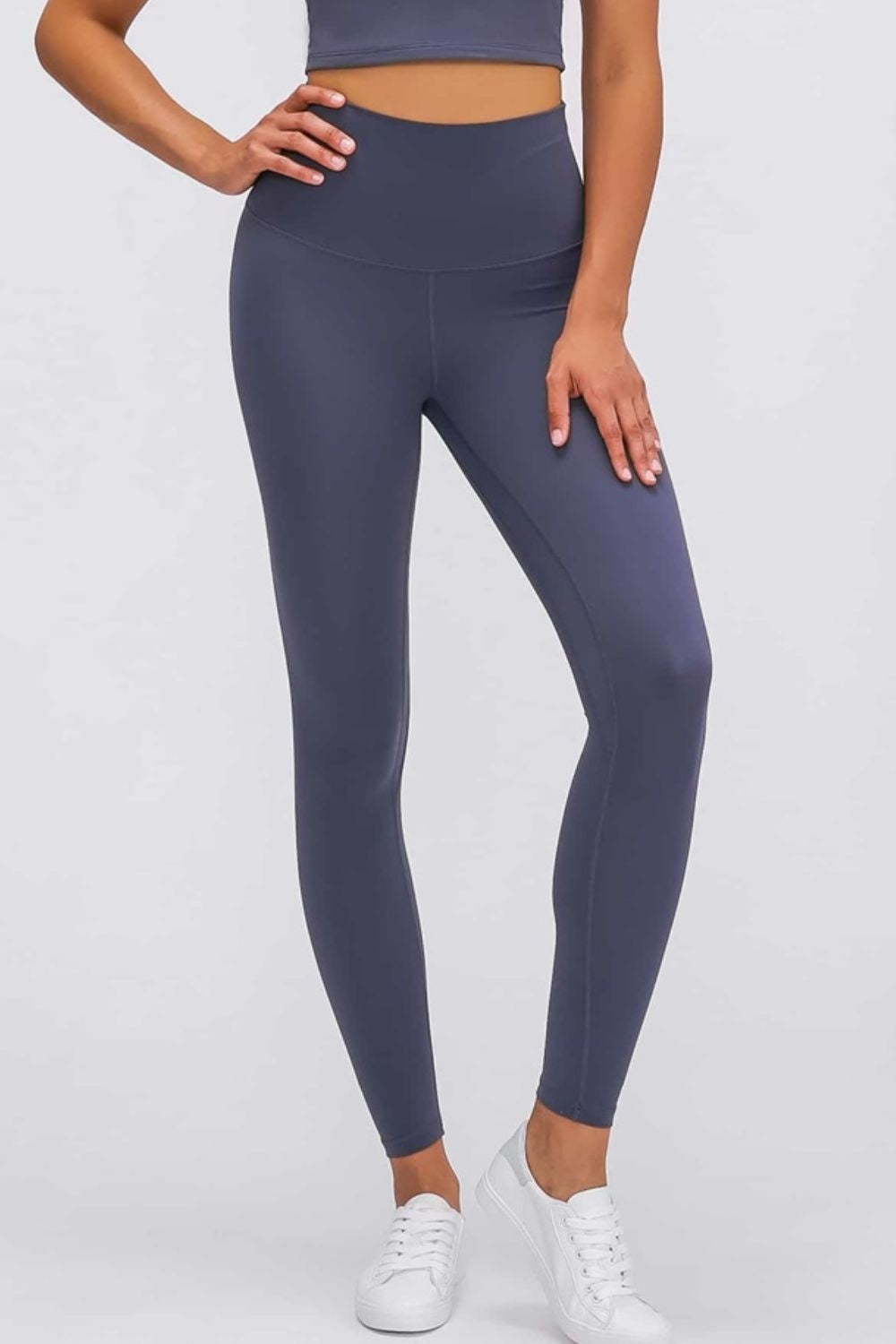Model poses in charcoal gray high-waist leggings with a smooth, stretchy, fitted silhouette, wide elastic waistband, visible seams, and ankle-length hems.