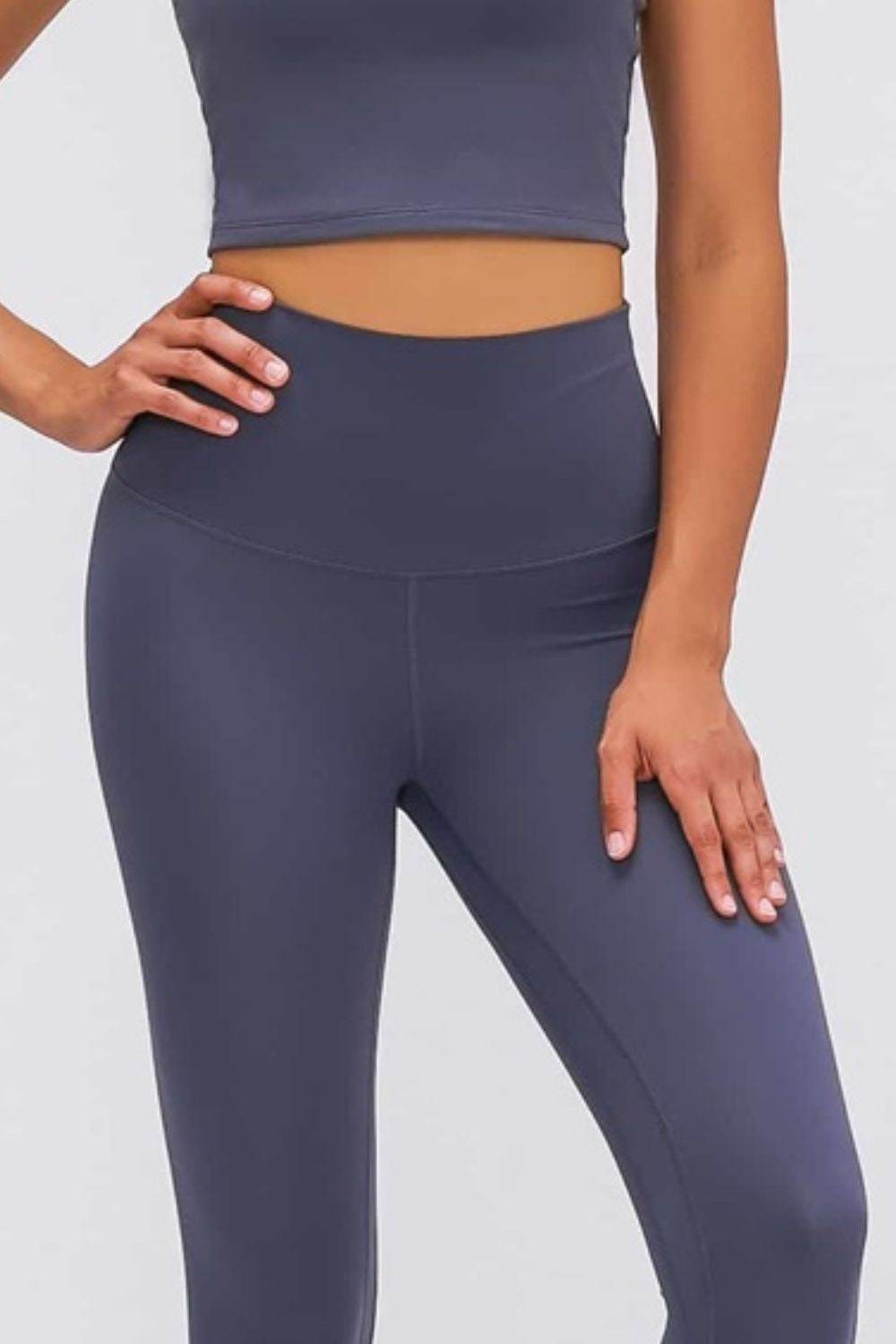 A model poses with one hand on her hip and one on her thigh, showcasing solid dark navy high-waisted leggings with a wide elastic waistband and fitted silhouette.