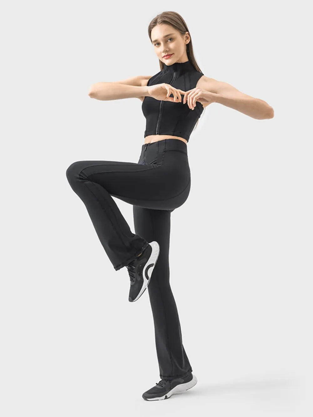 Model balances on one leg in black zipper detail high waist active pants with a sleek, fitted silhouette and gently flared hems.