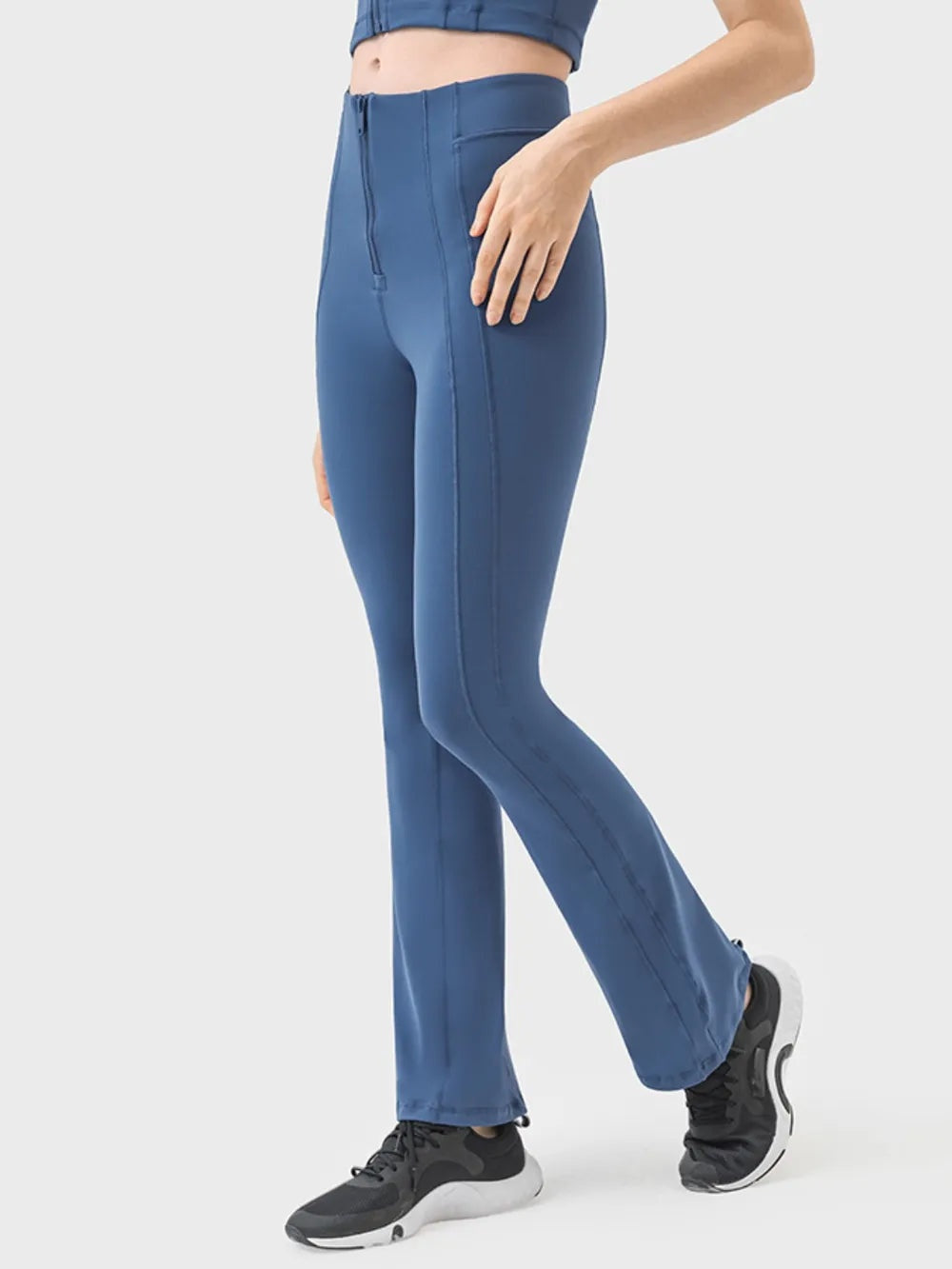 Model poses in blue high-waist active pants with front zipper detail, vertical seaming, a fitted straight-leg silhouette, and slight stretch.