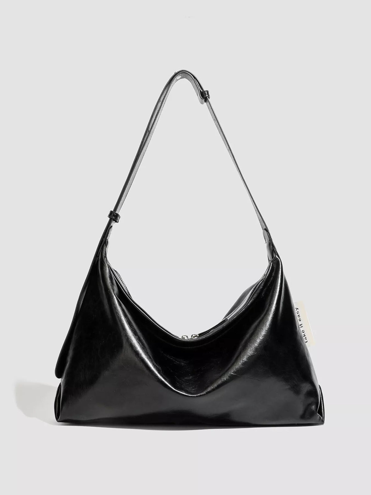 Glossy black PU leather shoulder bag with a slouchy silhouette, softly gathered sides, a curved top opening, and a long adjustable strap.