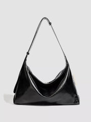 Glossy black PU leather shoulder bag with a slouchy silhouette, softly gathered sides, a curved top opening, and a long adjustable strap.
