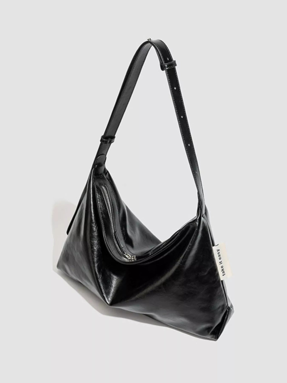 Medium black glossy PU leather slouchy shoulder bag with a relaxed silhouette, adjustable strap, and visible zippered pocket.