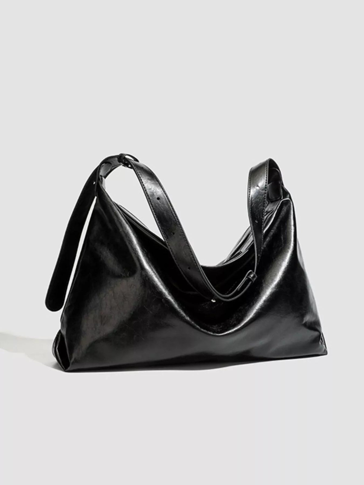 Glossy black PU leather shoulder bag with a slouchy medium silhouette, wide strap, softly folded construction, and a gently curved top opening.