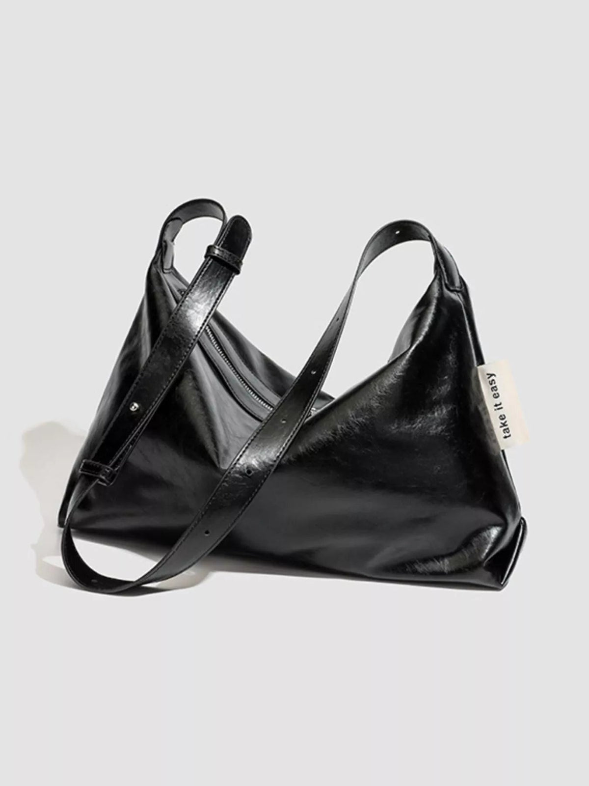 Black glossy PU leather slouchy shoulder bag with a relaxed silhouette, long adjustable strap, top zipper closure, and structured side seams.