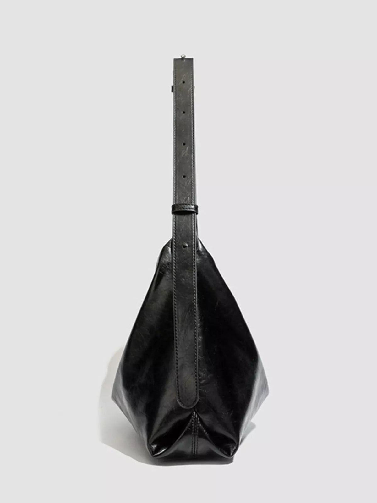 Black glossy PU leather slouchy shoulder bag with a medium gathered silhouette, long adjustable strap, and visible stitched construction.