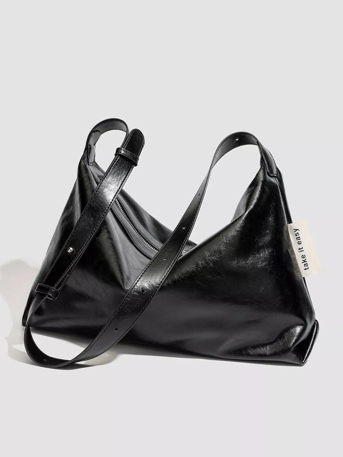 A medium black glossy PU leather slouchy shoulder bag features a soft triangular silhouette, long adjustable strap, and zippered top.
