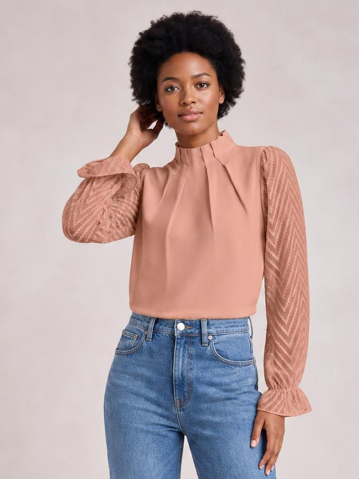 Model poses in a dusty rose mock neck blouse with flounce sleeves, ruffled cuffs, and semi-sheer patterned sleeves in a relaxed silhouette.