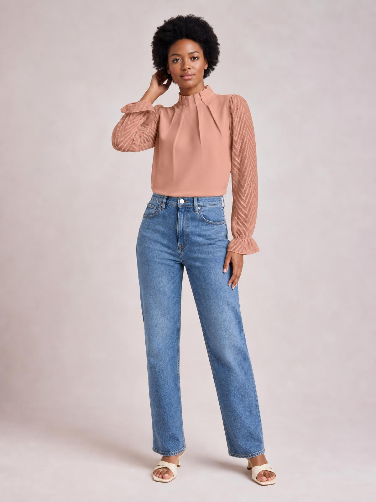 Model poses in a blush mock neck blouse with ruffled flounce sleeves, sheer chevron-textured panels, gathered cuffs, and a relaxed straight silhouette.