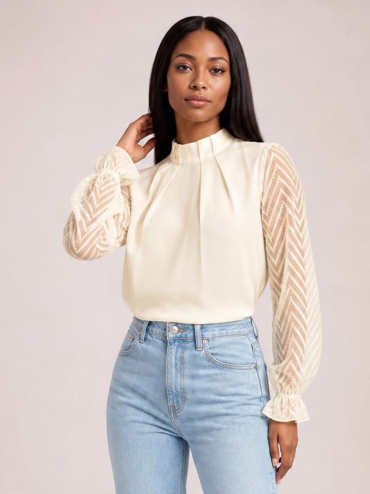 Model poses in a cream mock neck blouse with a relaxed silhouette, sheer chevron-patterned flounce sleeves, pleated front, and ruffled cuffs.