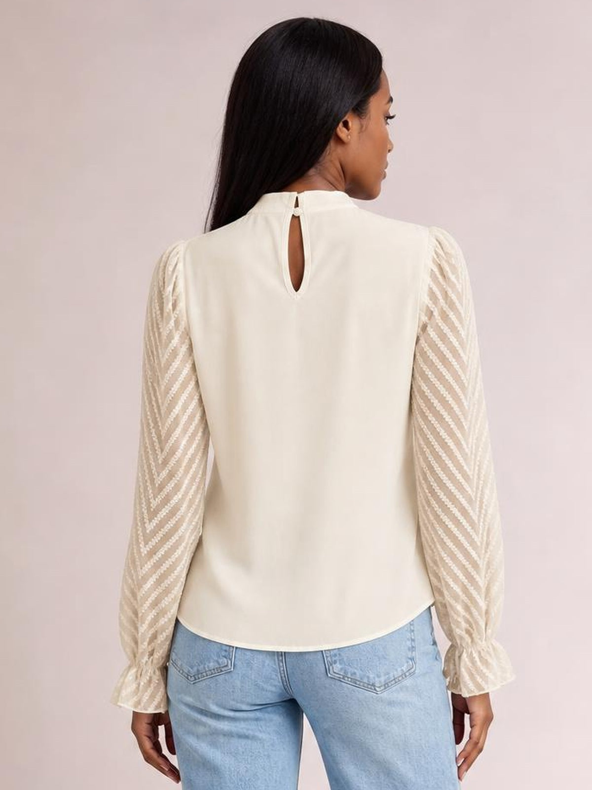 Model shown from behind wearing an ivory mock neck blouse with a keyhole back, relaxed silhouette, and semi-sheer diagonal-patterned flounce sleeves.