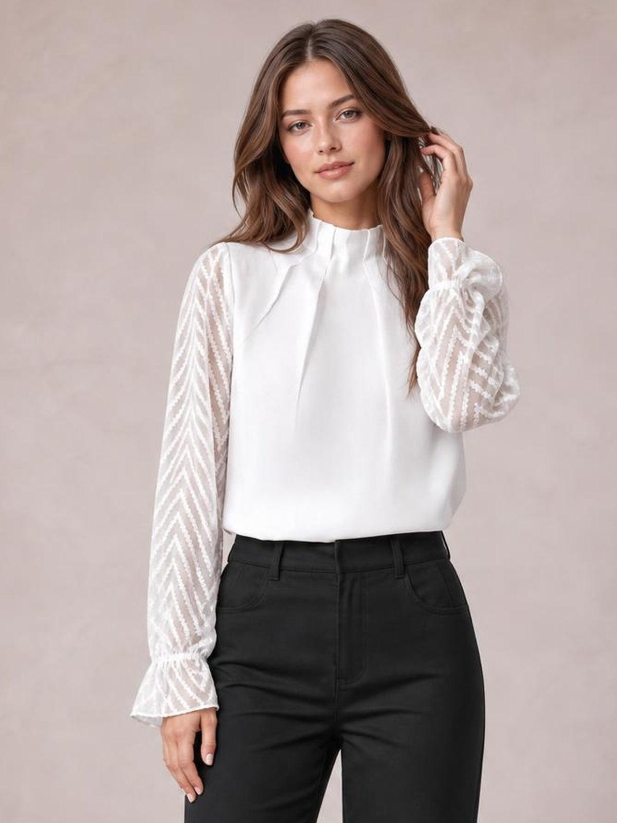 Model wearing a white mock neck blouse with a relaxed silhouette, semi-sheer patterned flounce sleeves, and ruffled cuffs, posing with one hand in her hair.