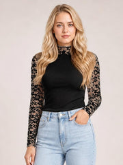 A model stands in a fitted black mock neck long sleeve t-shirt with semi-sheer floral lace patchwork sleeves and a sleek silhouette.