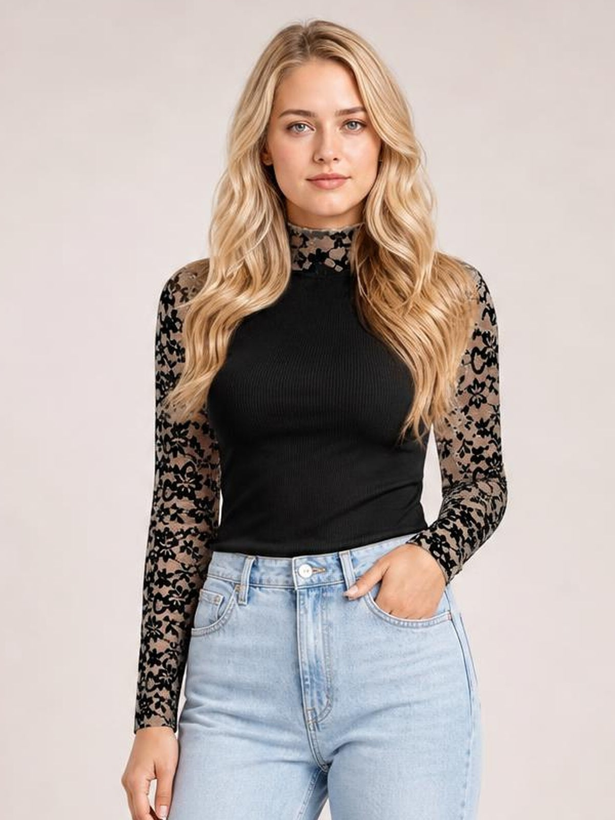 A model stands in a fitted black mock neck long sleeve t-shirt with semi-sheer floral lace patchwork sleeves and a sleek silhouette.