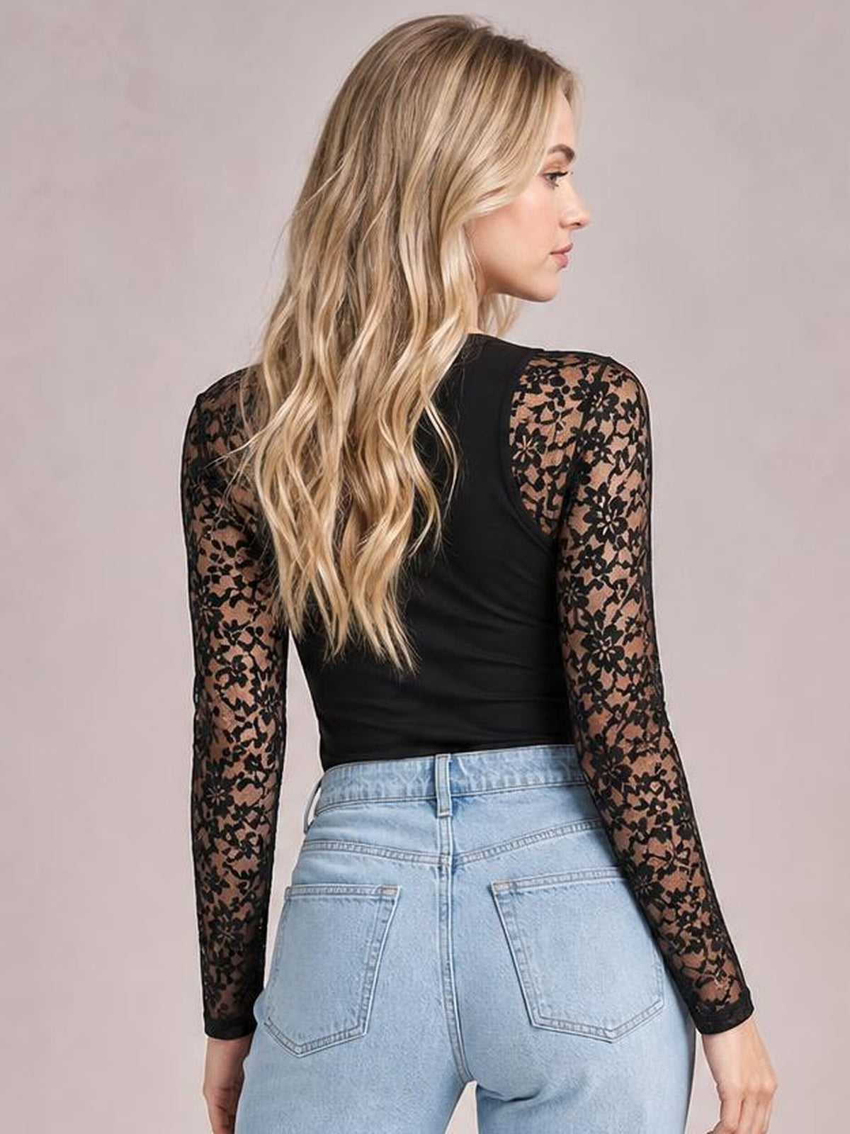 Model shown from the back in a black mock neck long sleeve t-shirt with semi-sheer floral lace patchwork sleeves and a fitted silhouette.