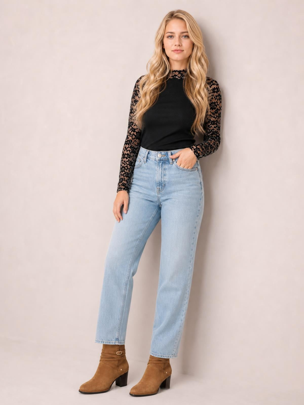 Model poses in a black mock neck long sleeve T-shirt with semi-sheer floral lace patchwork sleeves and a fitted silhouette, paired with light-wash jeans.