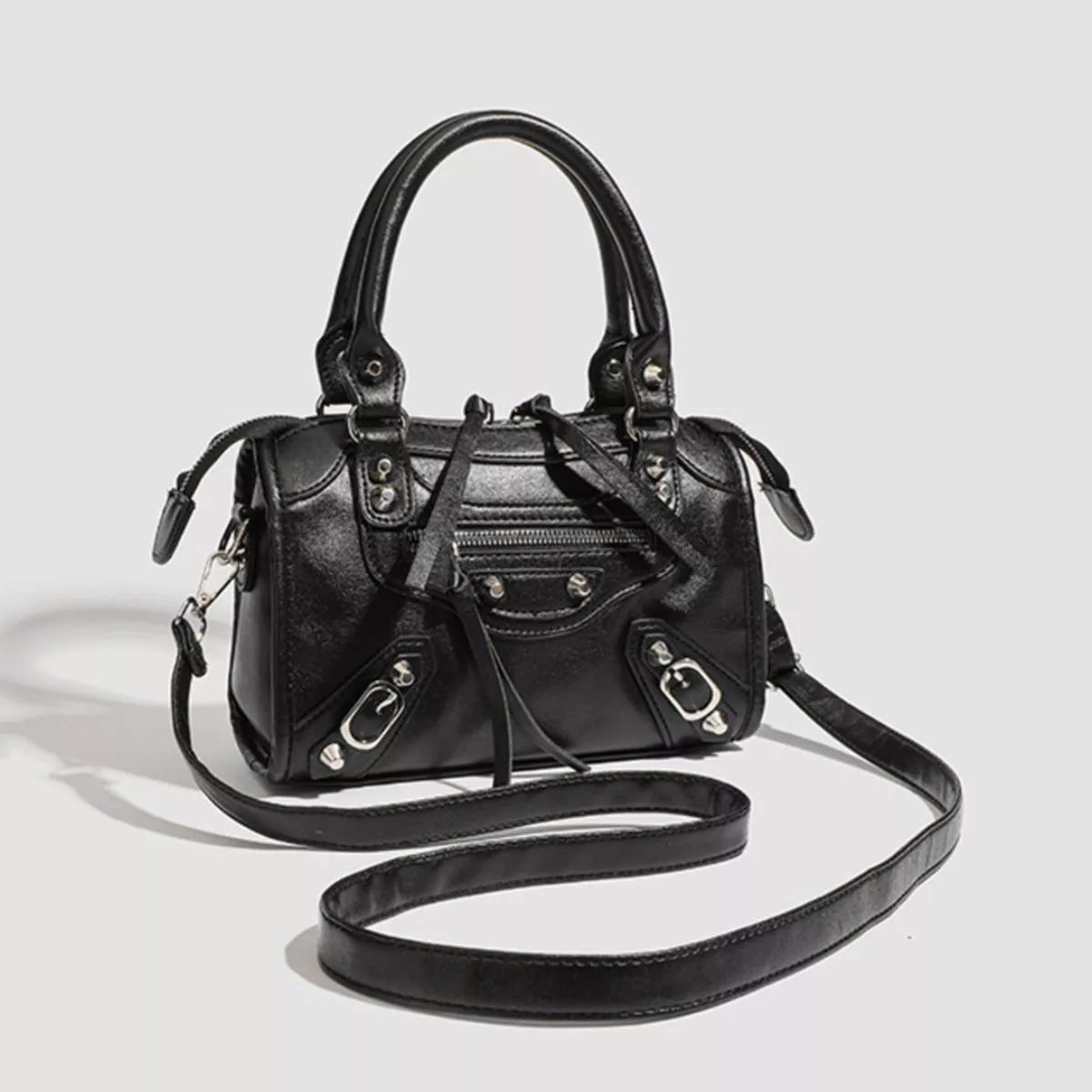 Small black PU leather motorcycle-style crossbody bag with top handles, silver-tone hardware, a front zip pocket, buckle accents, and a long strap.