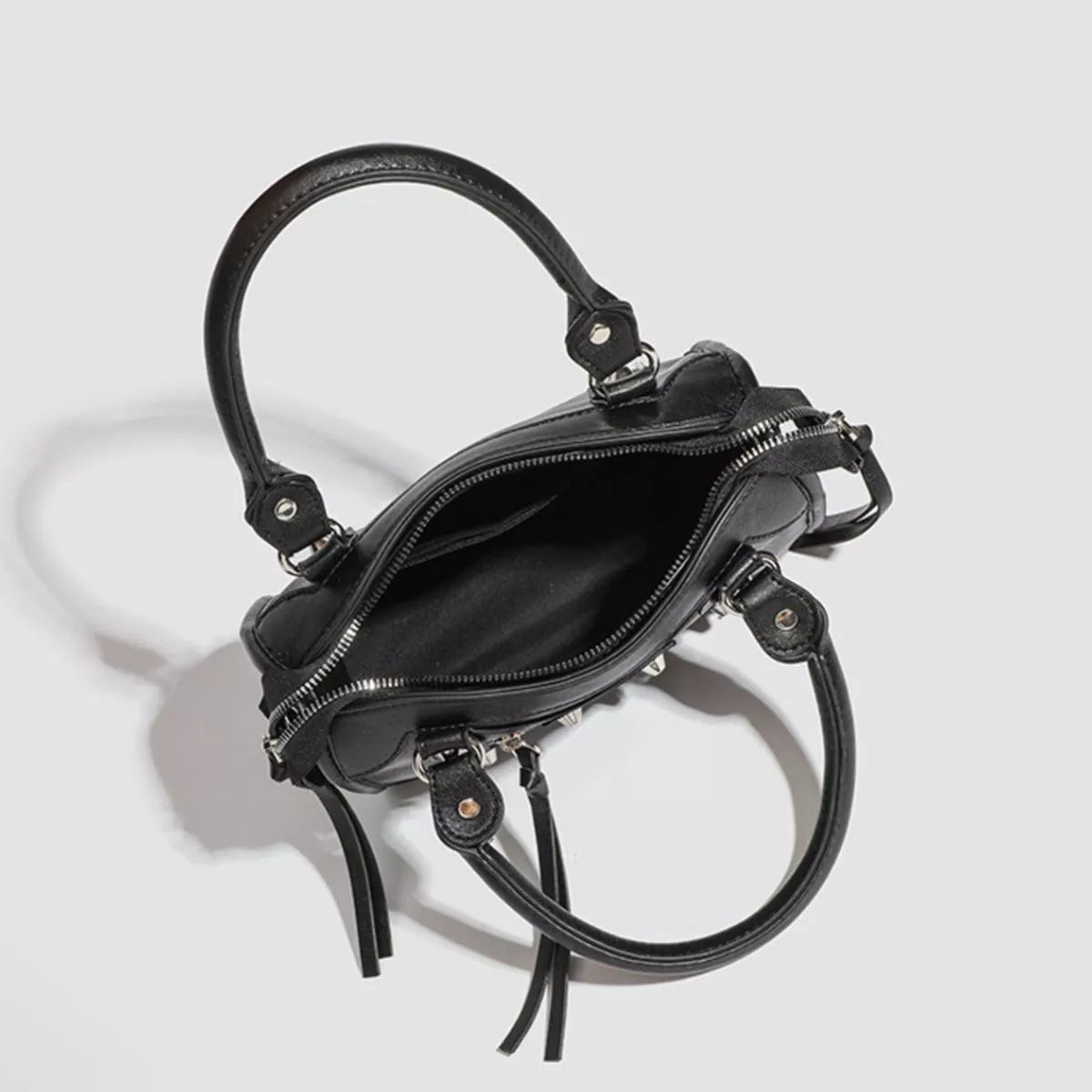 Small black PU leather crossbody bag with dual rounded handles, an open zippered top compartment, metal hardware, and long adjustable strap tabs.