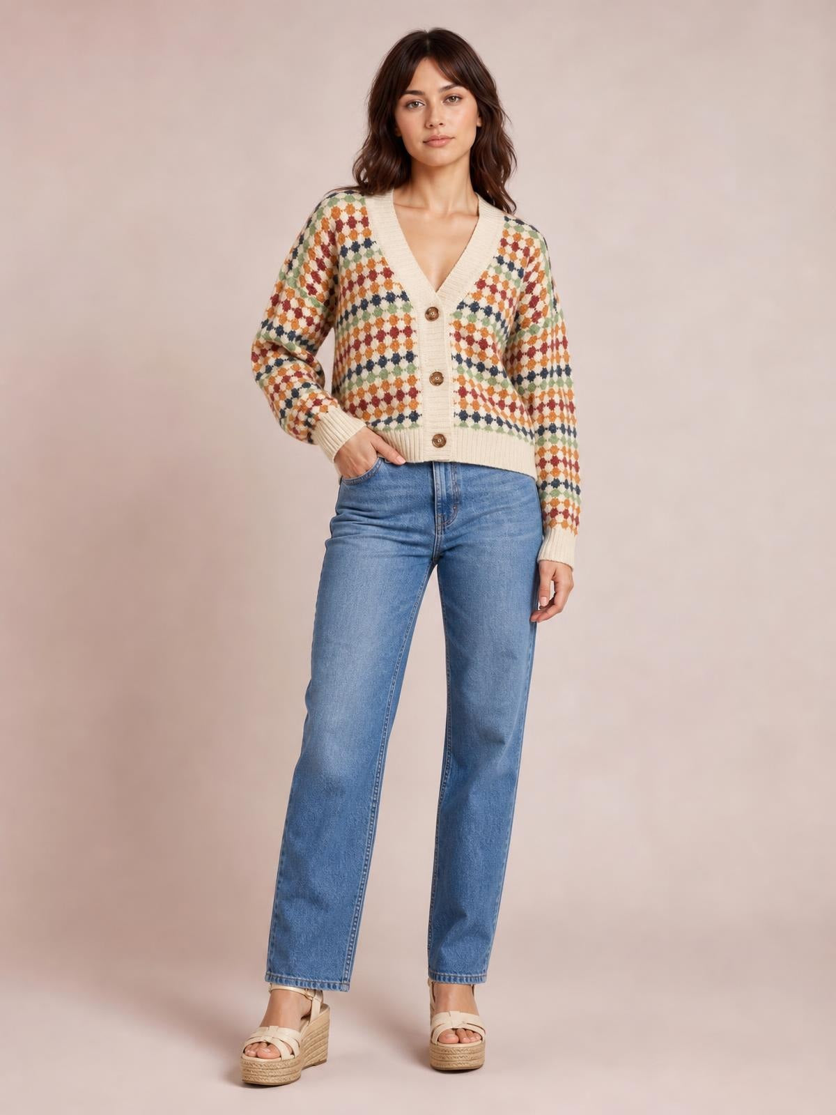 A model poses with one hand in her jeans pocket wearing a cream multicolour dotty knit cardigan with a V-neck, button front, long sleeves, and ribbed trim.