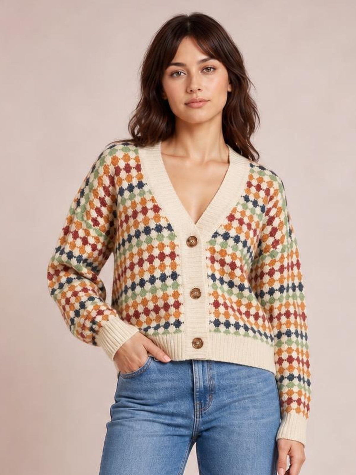 A model poses with one hand in her jeans pocket, wearing a cream multicolour dotty knit cardigan with a V-neck, button front, ribbed cuffs and hem.