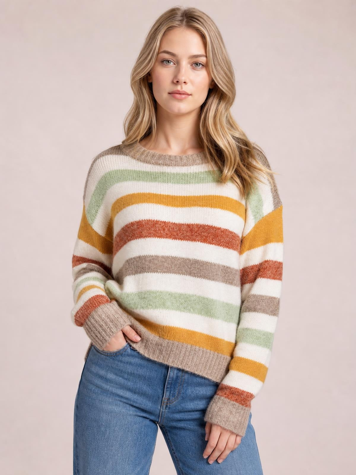 Model wearing a multicolour stripe drop shoulder crew neck sweater with ribbed beige trim, relaxed silhouette, and one hand tucked into jeans.