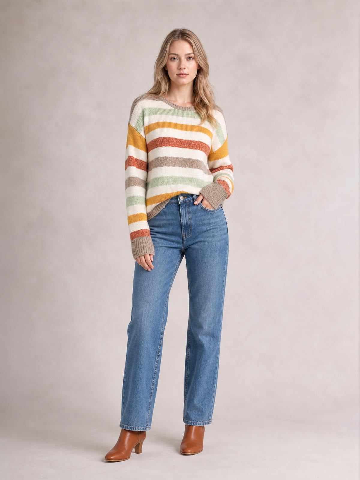 Model wearing a multicolour stripe crew neck sweater with drop shoulders, ribbed cuffs and hem, relaxed silhouette, and one hand in a jean pocket.