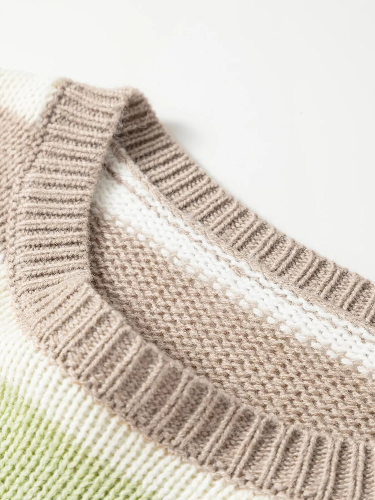 Close-up of a ribbed knit sweater in multicolour stripes, showing beige, white, and pale green sections with textured construction.
