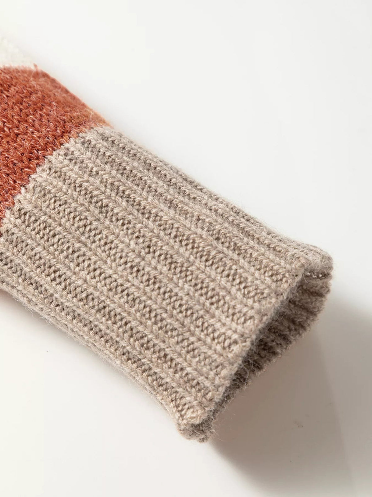 Close-up of the multicolour stripe sweater showing soft beige ribbed knit fabric with a rust-toned stripe and folded garment construction.
