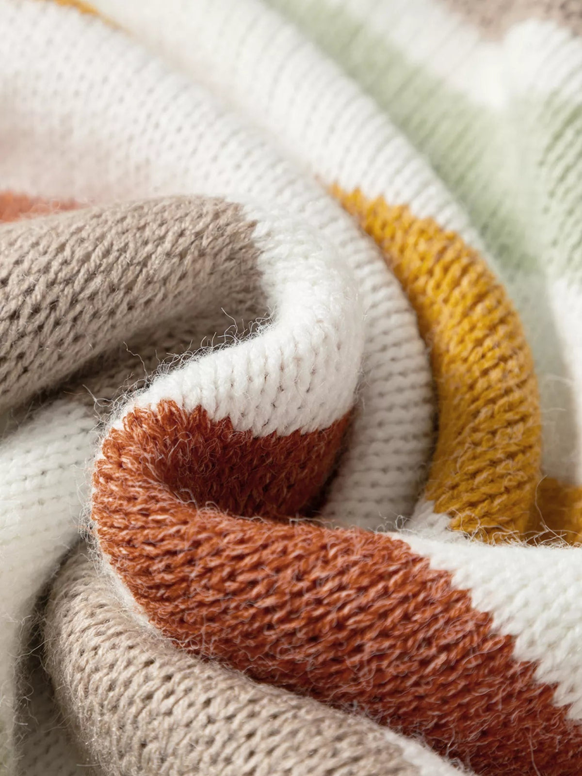 Close-up of a multicolour stripe knit sweater in cream, taupe, rust, and mustard, highlighting its soft textured ribbed construction.