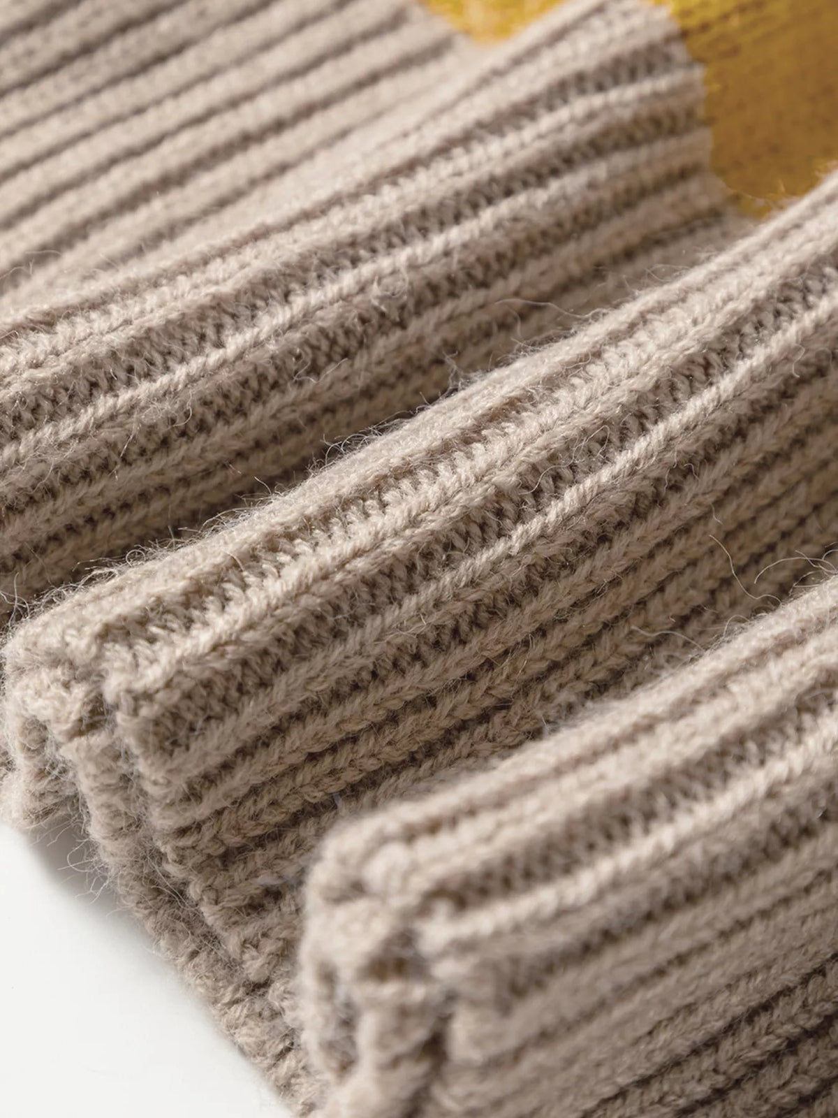 Close-up of a ribbed knit sweater in soft cream, taupe, and gray stripes, showing its fuzzy textured construction and subtle stretch.