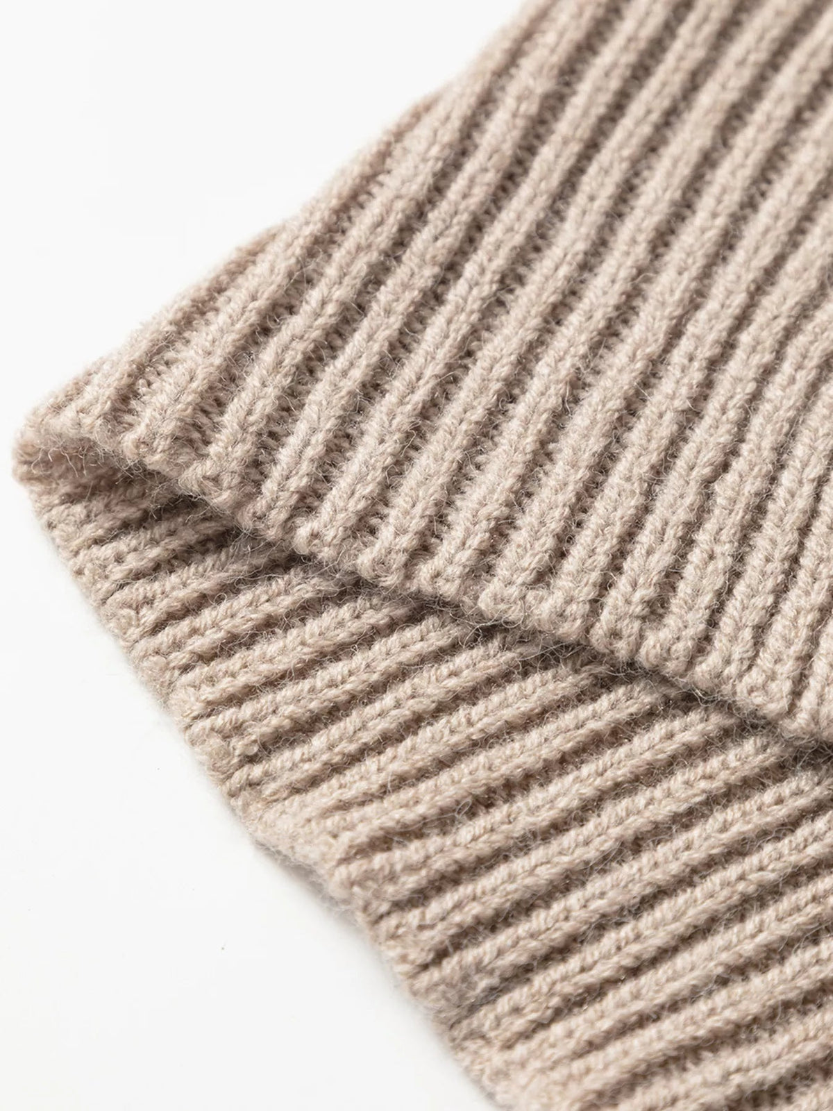 Close-up of the sweater’s soft beige ribbed knit, showing textured vertical ridges and a neatly finished folded edge.