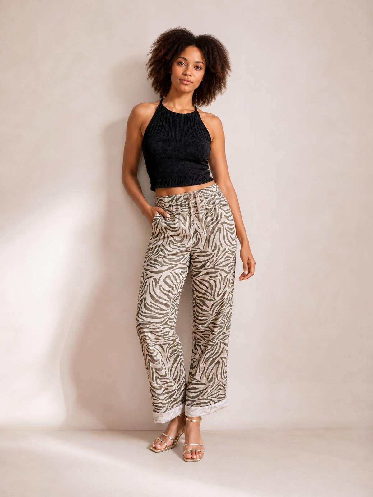 Model poses with one hand in the pocket wearing multicolour beige and black zebra-pattern pants with an elastic drawstring waist, relaxed straight legs, and cuffed hems.