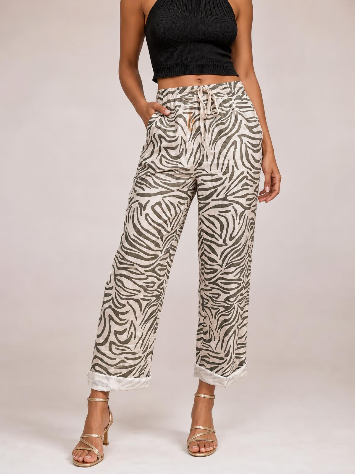 Model wears multicolour zebra-pattern pants with a drawstring elastic waist, side pockets, wide legs, and rolled cuffs while posing with one hand in a pocket.