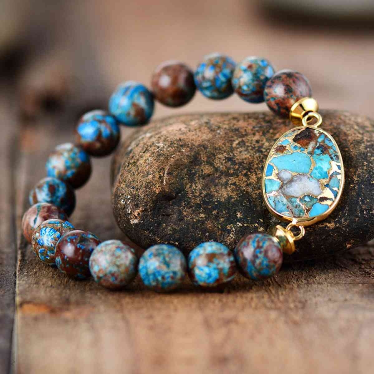 Natural stone beaded bracelet with round blue and brown patterned beads and a gold-tone oval stone pendant with a marbled finish.
