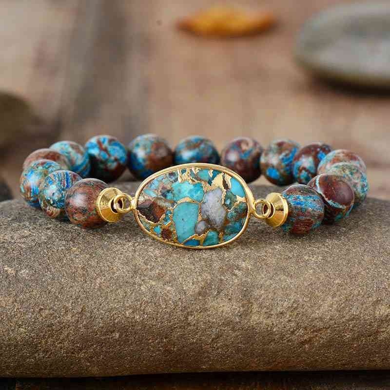 Natural stone beaded bracelet with round blue, brown, and burgundy beads and a gold-tone oval stone centerpiece in a bold stretch silhouette.