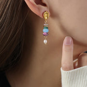 Close-up of a model wearing a gold-tone dangle earring with stacked colorful natural stone beads and a freshwater pearl drop, shown beside a knit sleeve.