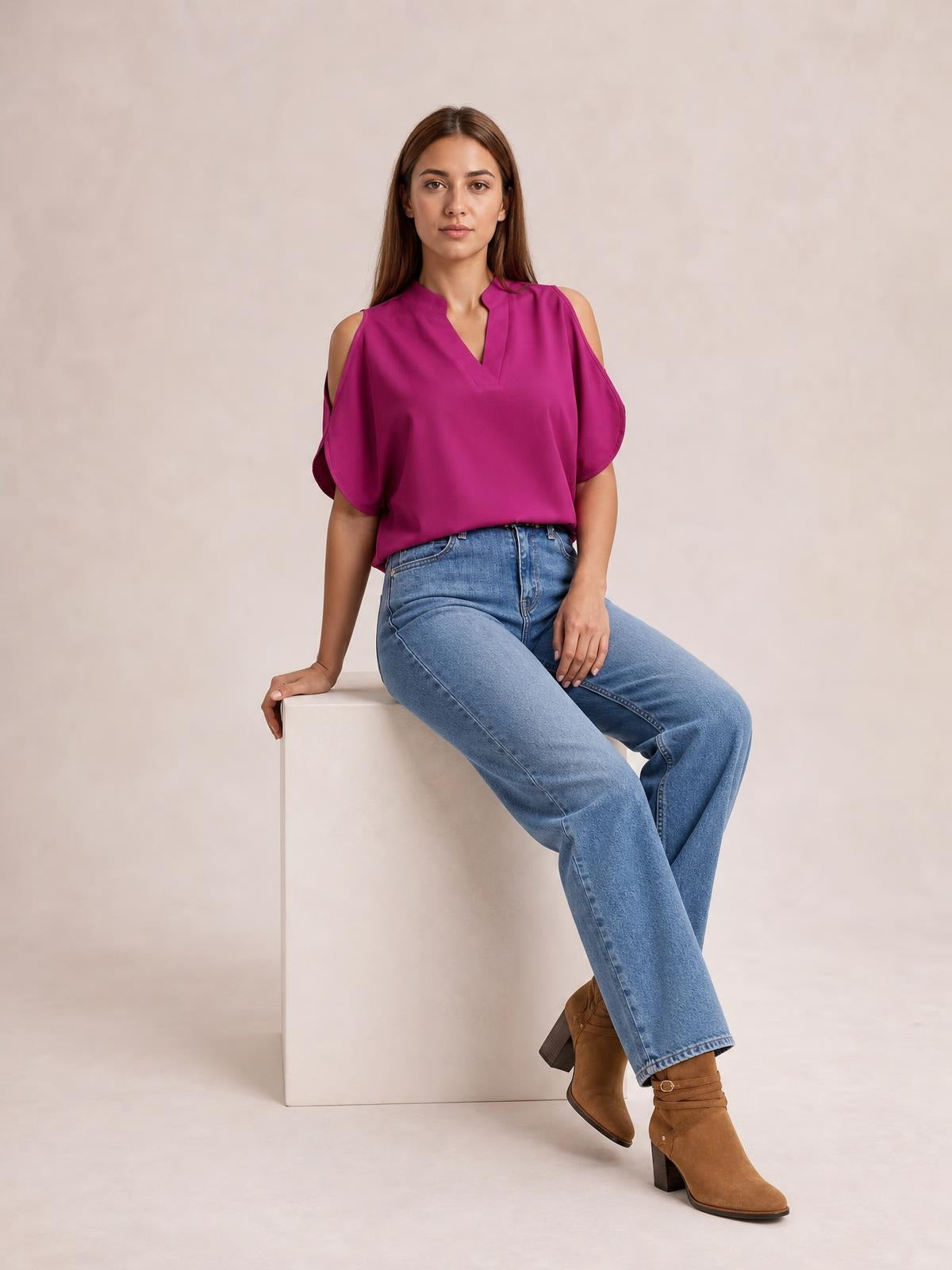 Model seated in a magenta notched cold shoulder blouse with a relaxed silhouette, V-neckline, and short draped sleeves.
