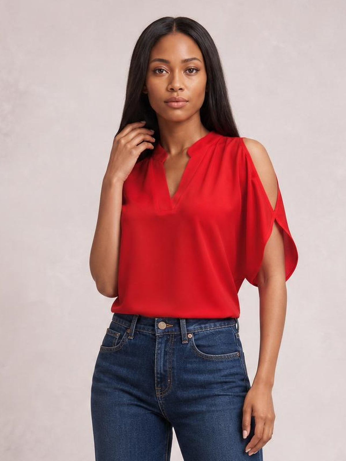 A model poses in a bright red notched cold shoulder blouse with a relaxed silhouette, draped short sleeves, and shoulder cutouts, paired with jeans.