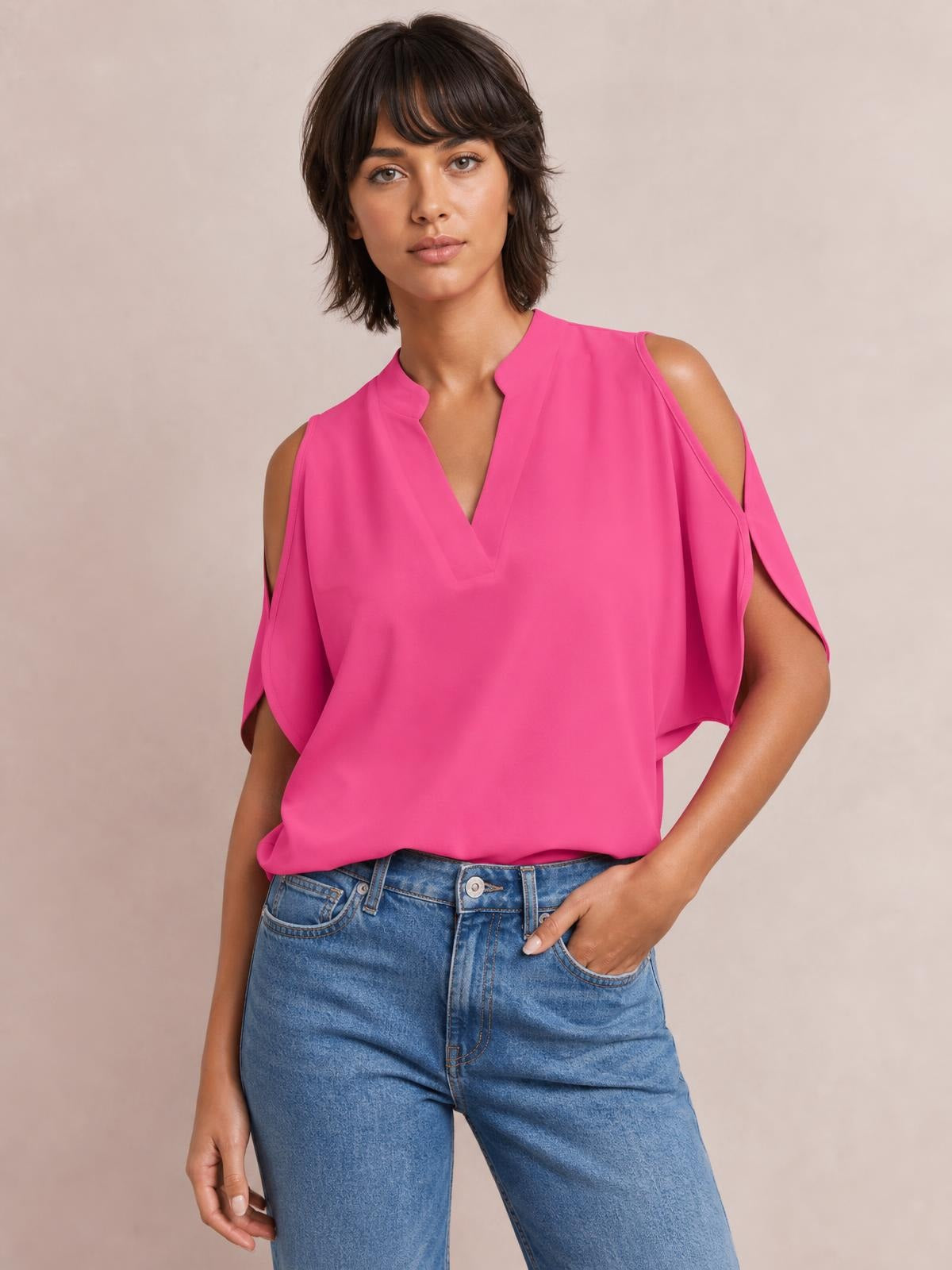 A model wears a bright pink notched cold shoulder blouse with a V-neckline, open shoulder cutouts, draped short sleeves, and a relaxed silhouette.