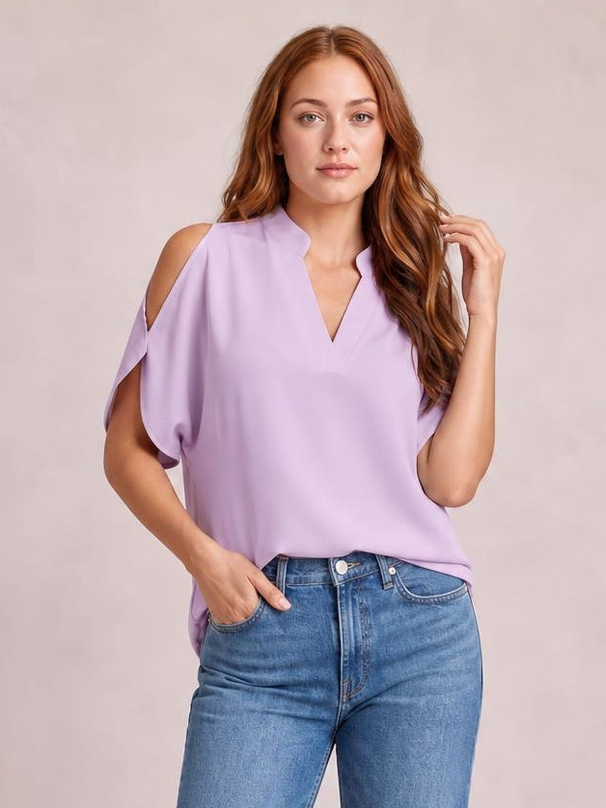 Model poses in a lavender notched cold shoulder blouse with an opaque, relaxed silhouette, short draped sleeves, and exposed shoulders.