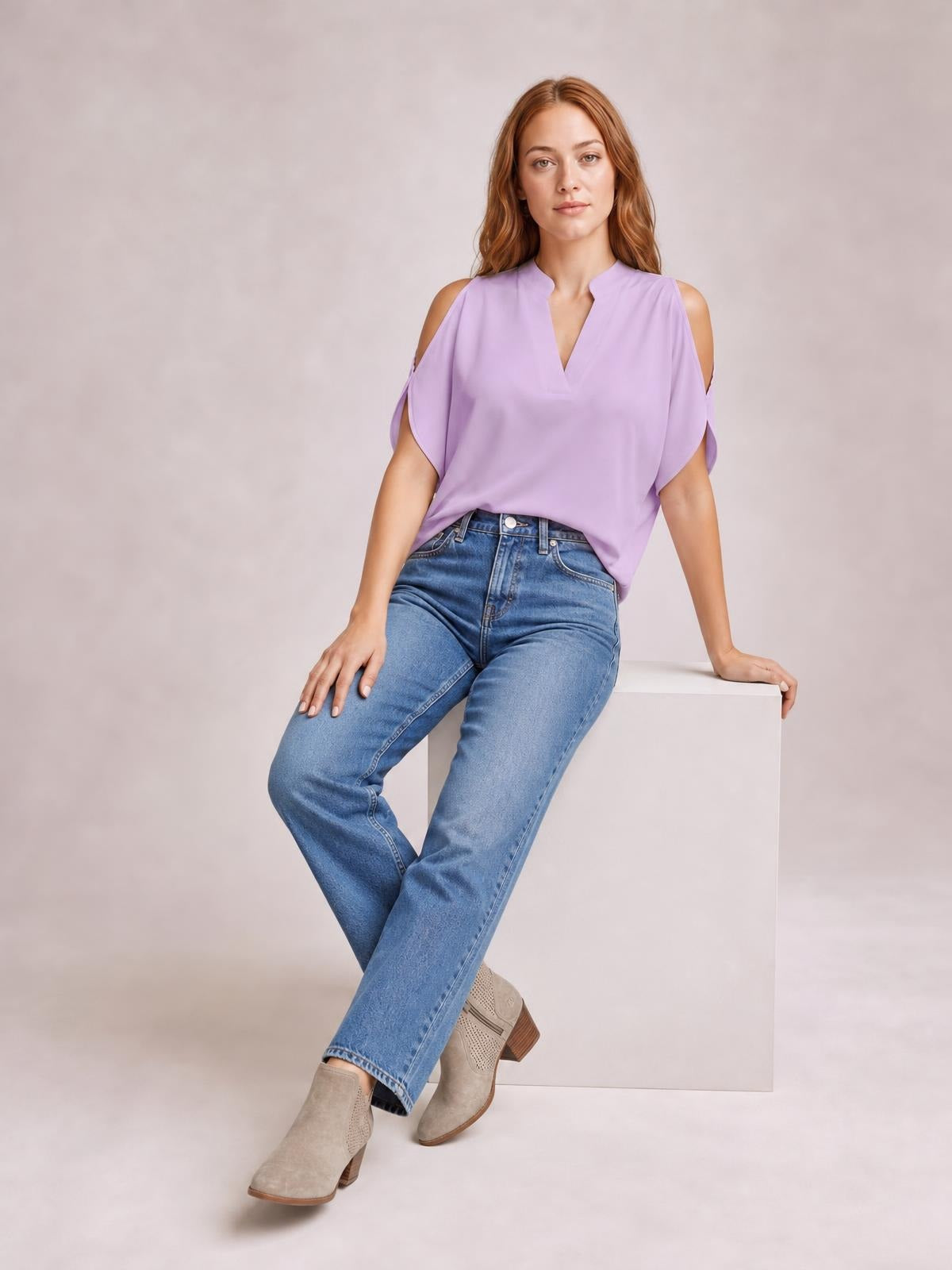Model seated in a lavender notched cold shoulder blouse with an oversized draped silhouette, short sleeves, and shoulder cutouts.