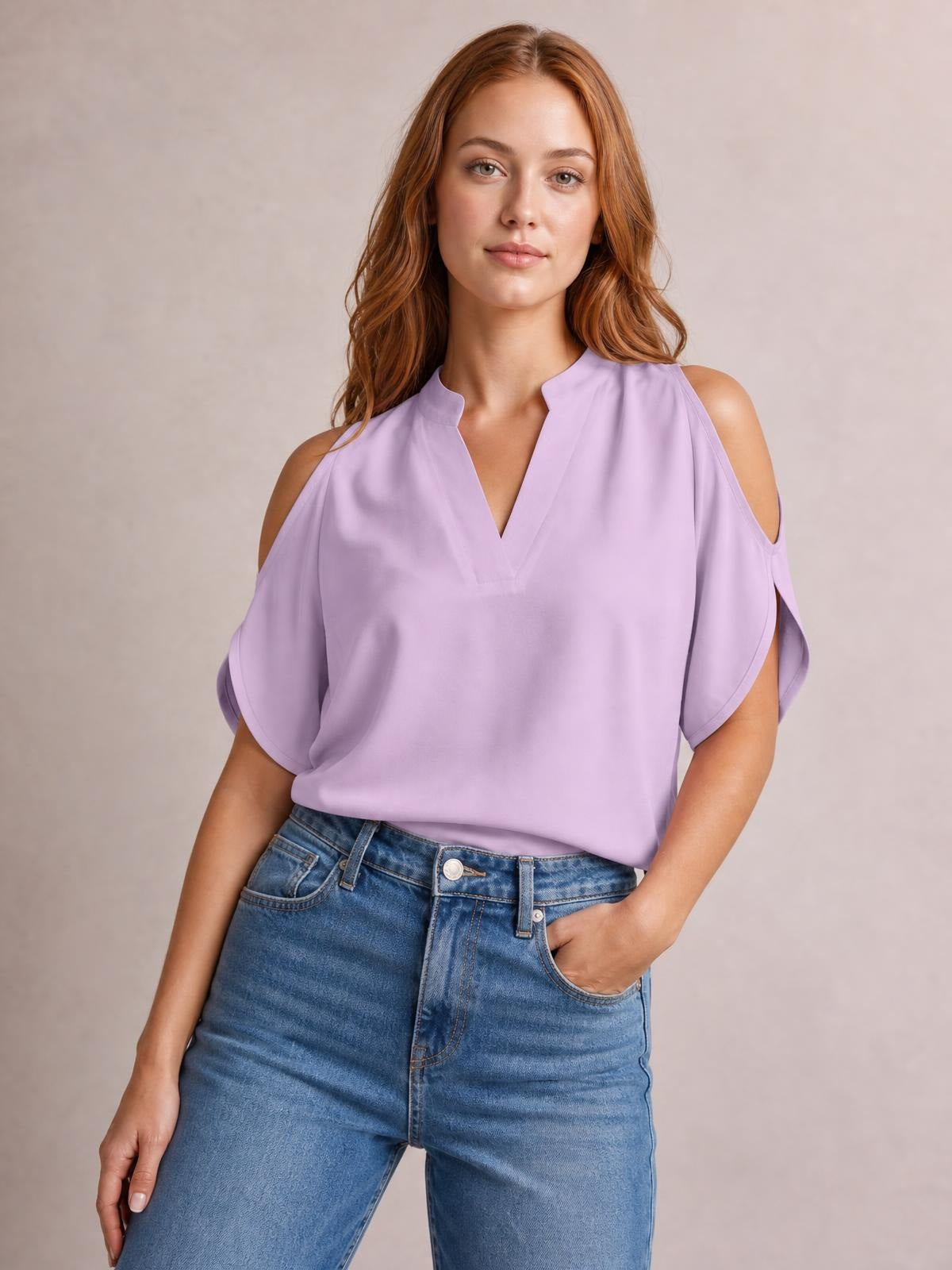 A model poses with one hand in her jeans pocket wearing a lilac notched cold shoulder blouse with a relaxed silhouette and draped short sleeves.