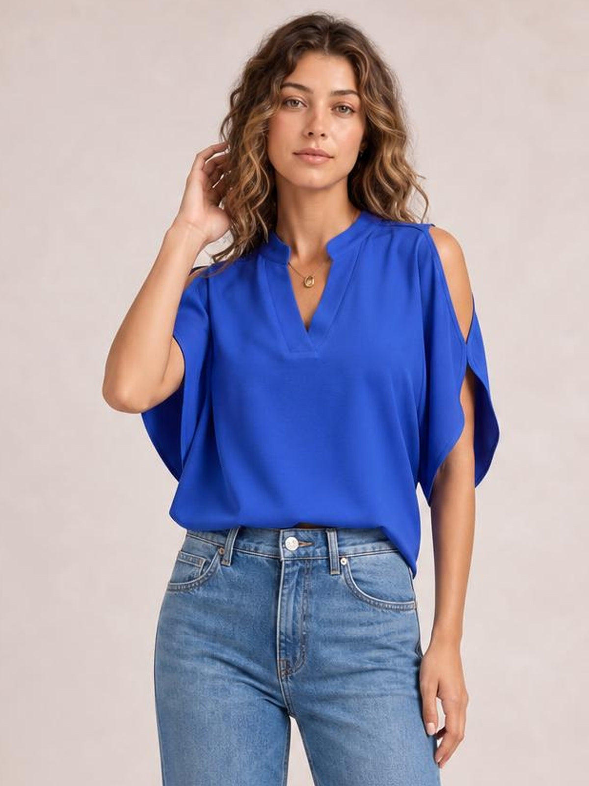A model poses in a bright blue notched cold shoulder blouse with a V-neckline, open shoulder cutouts, draped sleeves, and a relaxed silhouette.
