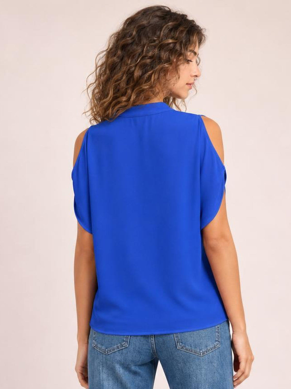 Model poses in a royal blue Notched Cold Shoulder Blouse with exposed shoulders, short sleeves, a relaxed straight silhouette, and a smooth opaque finish.