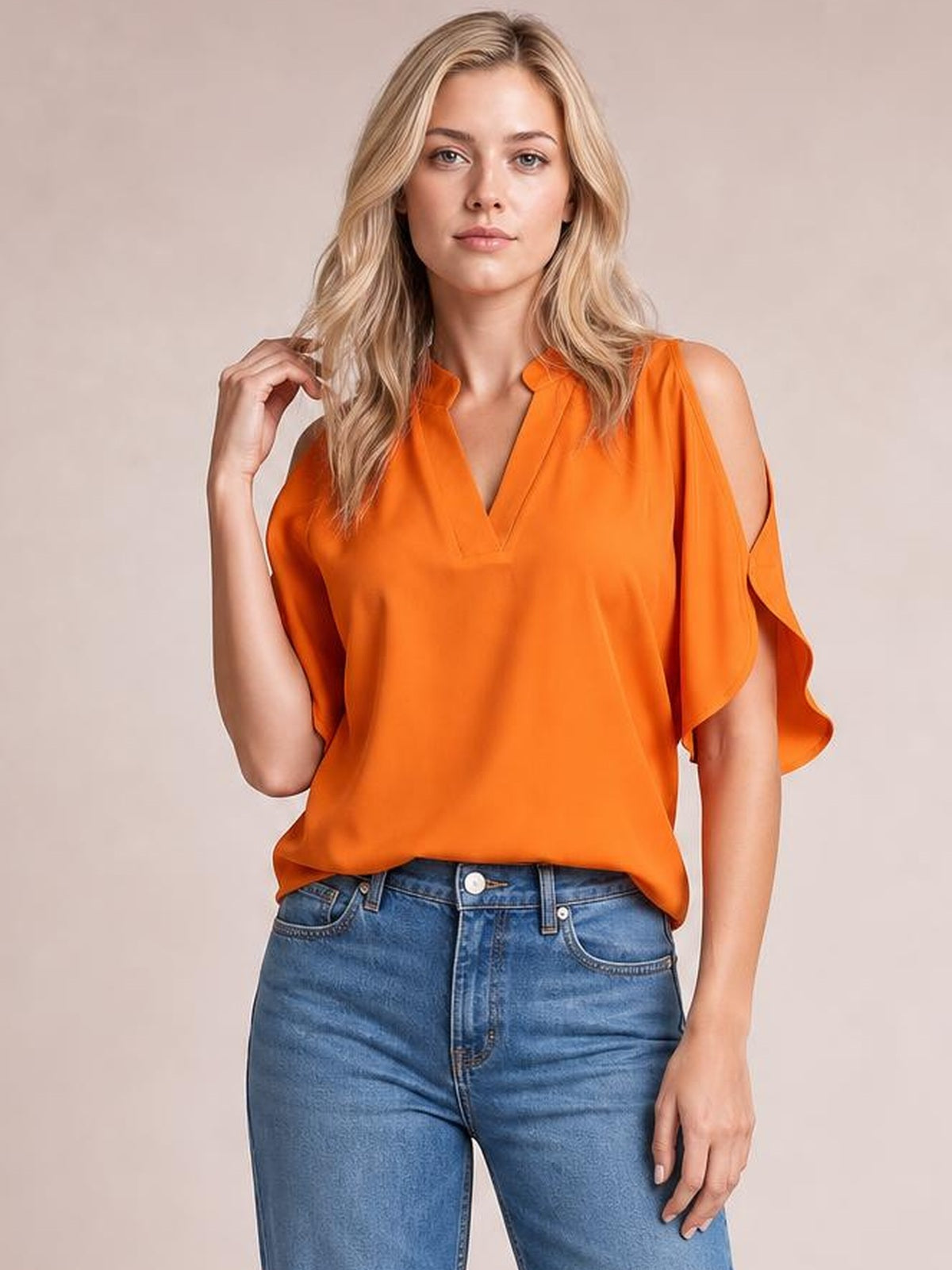 Model wearing an orange notched cold shoulder blouse with a relaxed, loose silhouette and flowing cutout sleeves, posing with one hand near her hair.